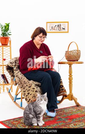 Großmutter strickt in Quarantäne auf Nadeln, daneben sitzt eine graue Katze Stockfoto
