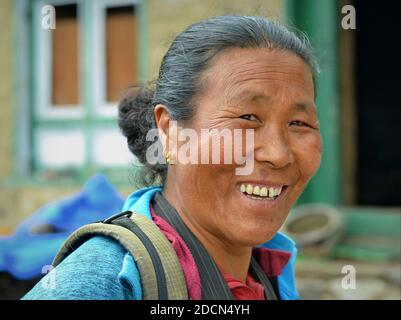 Glückliche, ältere Nepalesin tibetischer Herkunft lächelt für die Kamera vor ihrem Dorfhaus. Stockfoto