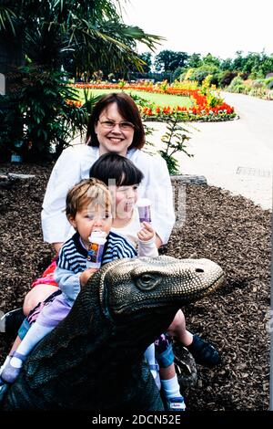 Eine Familie, eine Frau und zwei Mädchen sitzen auf einer Bronze-Comodo-Drachenskulptur im Chester Zoo, Großbritannien Stockfoto