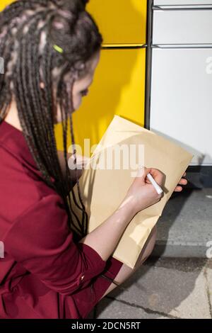 Er sucht geistig nach der genauen Korrespondenzadresse. Er schreibt mit einem weißen Stift auf einen Umschlag. Schreibt den Adressaten. Stockfoto