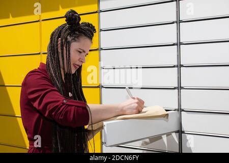 Er sucht geistig nach der genauen Korrespondenzadresse. Er schreibt mit einem weißen Stift auf einen Umschlag. Schreibt den Adressaten. Stockfoto