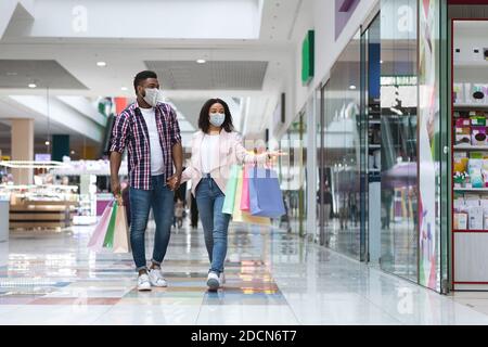 Junge schwarze Paar trägt schützende medizinische Gesichtsmaske zu Fuß in Einkaufszentrum Stockfoto