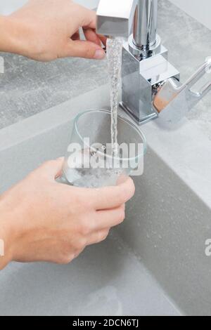 Hand hält ein Glas Wasser aus der Küche Wasserhahn gegossen. Trinkwasser sparen