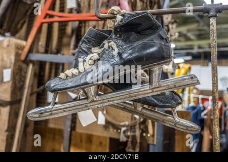 Ein paar alte gebrauchte abgenutzte Schlittschuhe hängen Auf einer Rute in einem Keller lange vergessen von umgeben Andere Unordnung im Hintergrund drinnen Stockfoto