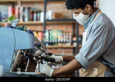 Der professionelle Barista arbeitet während der sozialen Distanzierung mit der Ausrüstung im Café Stockfoto