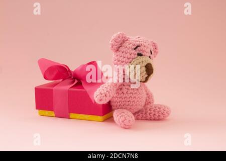 Kleiner Häkelbär in pink mit einer Geschenkbox auf der Rückseite. Rosa Farbe. Liebeskonzept. Stockfoto