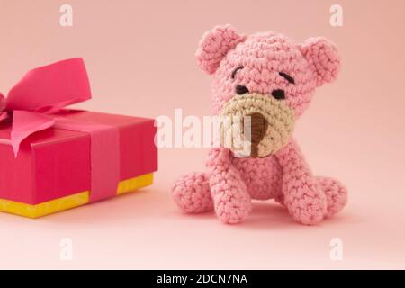 Kleiner Häkelbär in pink mit einer Geschenkbox auf der Rückseite. Rosa Farbe. Liebeskonzept. Stockfoto