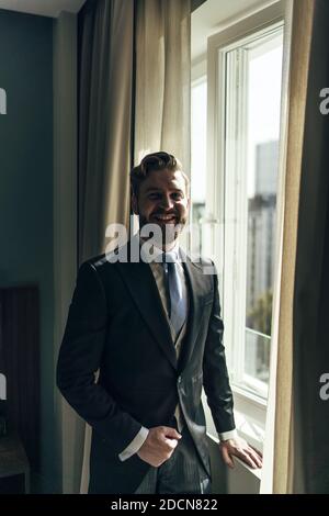 Ein flacher Fokus eines erwachsenen Mannes mit Bart In einem eleganten Anzug und in der Nähe der Fenster Stockfoto