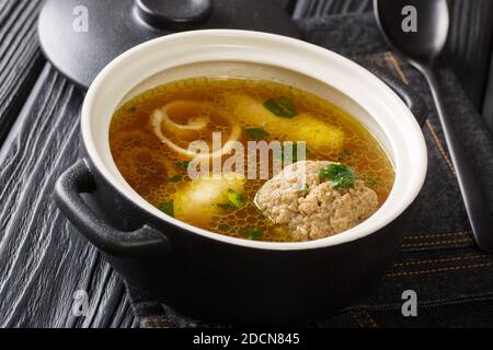 Köstliche Wiener Rindsuppe auf der Basis von Rinderbrühe mit Knödeln aus der Nähe in einem Topf auf dem Tisch. Horizontal Stockfoto
