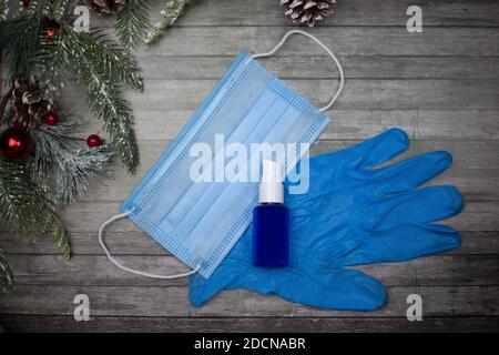 Maske, Handschuhe und Antiseptikum liegen auf einem hölzernen Hintergrund und einem Zweig eines Weihnachtsbaums. Silvester ist in Quarantäne Stockfoto