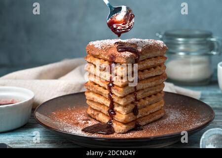 Herzförmige Wiener Waffeln mit Schokolade, Puderzucker und Erdbeersoße auf grauem Hintergrund. Stockfoto