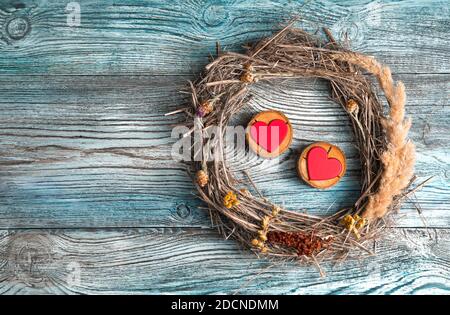 Zwei rote Herzen auf einem hölzernen Ständer in einem Rahmen aus trockenen Ästen und Gras auf einem hölzernen Hintergrund. Stockfoto