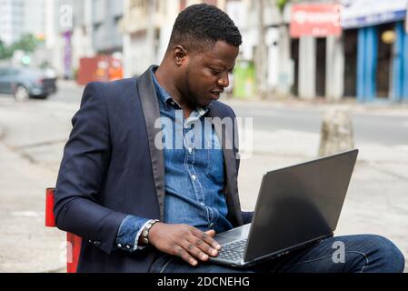 Der junge Mann sitzt in der Jacke und schaut lächelnd auf den Laptop. Stockfoto