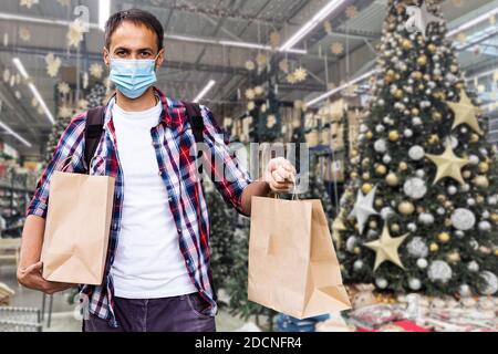 Ein Mann trägt eine medizinische Schutzmaske mit einem großen Geschenk, Weihnachtslieferung Stockfoto