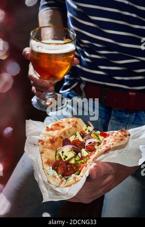 Ein Mann, der einen veganen Gyros isst, Horiatiki-Salat mit Koriander-Olivenöl und zerkleinerten Tomaten, auf Pita-Brot gesetzt. Stockfoto