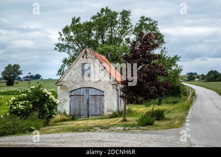 Altes verwittertes Ziegelgebäude mit abblätterndem Gips an einer kleinen Landstraße in Valleberga, Skane, Südschweden. Stockfoto