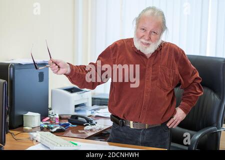 Europäische fröhliche und gutmütige Büroangestellte im Rentenalter ist Am Tisch an seinem Arbeitsplatz Stockfoto