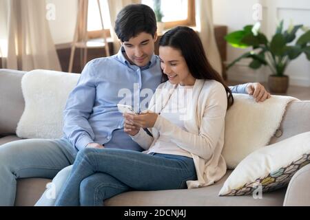 Glücklich liebende junge Familie Paar mit Handy auf der Couch Stockfoto