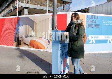 Brunette Frau Händewaschen in öffentlichen Händedesinfektionseinheit an Ort und Stelle für die aktuelle covid19 Pandemie. Kings Cross, London. Stockfoto