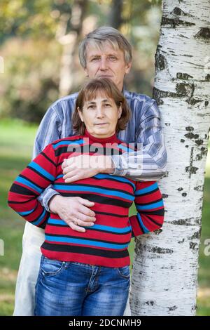 Älterer Ehemann umarmt seine Frau, während er in der Nähe von Birke steht Im Park Stockfoto