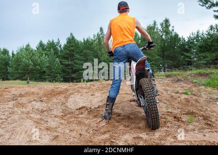 Mototrial junger Fahrer stehend mit Motorrad in Sand. Extremsport auf Motorcross-Motorrad. Rückansicht, Copyspace Stockfoto