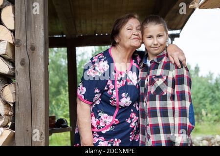 Die alte Großmutter küsst zwölf alte Enkelin, Portrait auf der Veranda des hölzernen Sommerhauses, zwei Personen Stockfoto