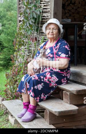 Landsfrau hält haarlose sphynx Katze auf den Knien, wenn sie sitzt Auf Holzveranda Stockfoto