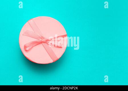 Runde rosa Geschenkbox mit Band und Schleife auf türkisfarbenem Hintergrund mit Kopierfläche. Geschlossener Karton. Überraschung für einen Urlaub, Weihnachten. Draufsicht, fl Stockfoto