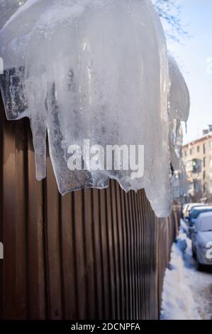 Große Eiszapfen auf dem Hintergrund eines Metallzauns. Gefahr von Eis auf Dächern und Zäunen während des Tauens. Stockfoto