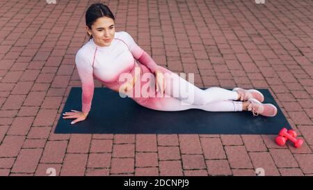 Schönes Mädchen mit einer sportlichen Figur sitzt auf einem Yoga Matte ruht nach intensivem Training Stockfoto