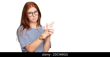 Junge Frau mit Lesekopf in legerer Kleidung und Brille, die symbolische Waffe mit Handbewegung hält, Tötung von Schusswaffen, wütendes Gesicht spielt Stockfoto