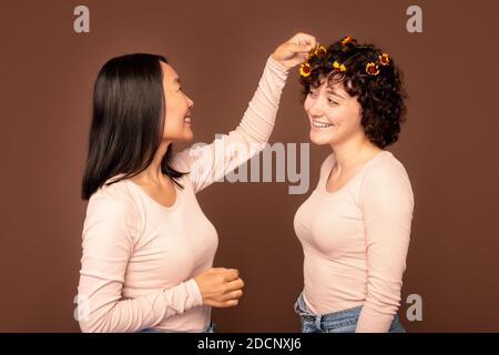 Eine von zwei jungen interkulturellen Frauen, die kleine Blumen hineinstecken Haare ihrer Freundin Stockfoto