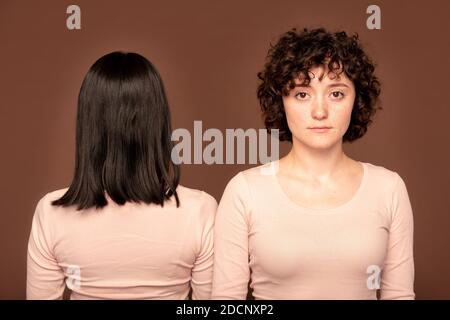 Junge ernsthafte Brünette Frau auf dem Hintergrund der Rückseite Eine weitere Frau Stockfoto