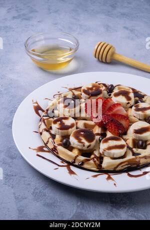 Ein vertikaler Schuss köstlicher Belgischer Waffeln mit Schokolade, Bananen und Erdbeeren auf einem Teller auf dem Tisch Stockfoto