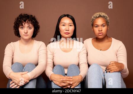 Gruppe junger ernster Weibchen verschiedener Ethnien sitzen darin Vorderseite der Kamera Stockfoto