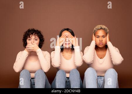 Drei junge hübsche Frauen in Casualwear, die Augen, Ohren und Mund bedecken Stockfoto