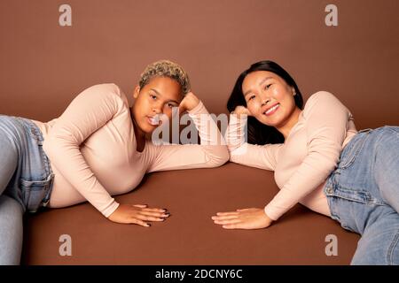 Zwei junge zeitgenössische Frauen verschiedener Ethnien in Jeans und Pullover Stockfoto