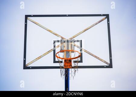 Basketballkorb mit transparentem Brett und Ketten statt Netz Gegen den hellblauen klaren Himmel am Nachmittag ab Einen vorderen unteren Winkel Stockfoto