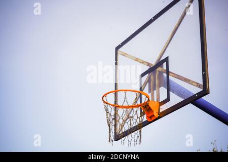 Basketballkorb mit transparentem Brett und Ketten statt Netz Gegen den hellblauen klaren Himmel am Nachmittag mit Eine leichte dunkle Vignette Stockfoto