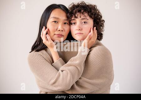 Liebevolle interkulturelle Mädchen in einem Pullover berühren Gesichter von einem Ein anderes Stockfoto