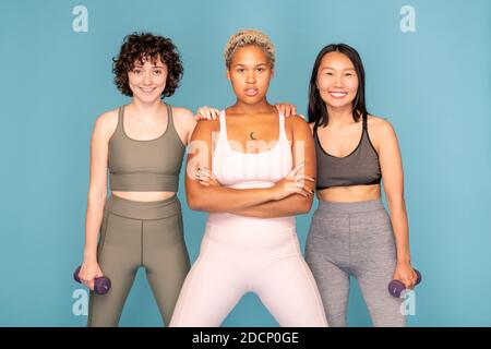 Zwei glückliche Sportlerinnen mit Hanteln stehen neben ihrer Mixed-Race-Hündin Freund Stockfoto