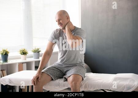 Kahlköpfiger Mann, der schmerzhaften Hals auf seiner linken Seite berührt und massiert Es vor dem Training Stockfoto