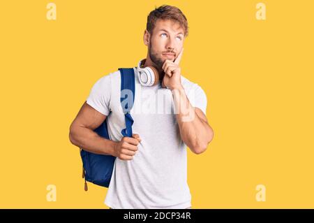 Junge kaukasische Mann trägt Student Rucksack und Kopfhörer ernstes Gesicht denken über Frage mit Hand auf Kinn, nachdenklich über verwirrende Idee Stockfoto