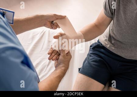 Hände des Arztes, die Handfläche und Handgelenk des kranken Patienten einwickeln Mit flexibler Bandage Stockfoto