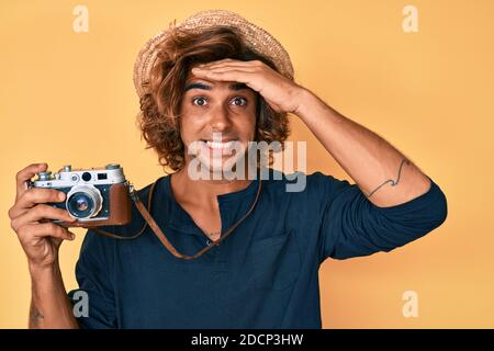 Junger hispanischer Mann mit Hut mit Vintage-Kamera gestresst und frustriert mit Hand auf Kopf, überrascht und wütend Gesicht Stockfoto