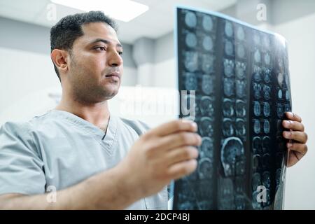 Zeitgenössische Mischrassen Radiologen in Uniform Blick auf Röntgenbild von Patient Stockfoto