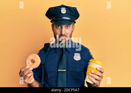 Handsome hispanic Polizeimann essen Donut und trinken Kaffee deprimiert und sorgen für Not, Weinen wütend und Angst. Trauriger Ausdruck. Stockfoto