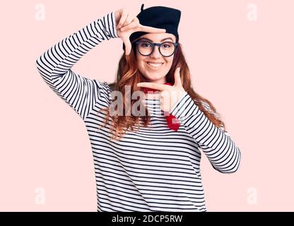 Junge schöne Frau trägt französisch Look mit Baskenmütze lächelnd machen Rahmen mit Händen und Fingern mit glücklichen Gesicht. Kreativität und Fotografie Konzept. Stockfoto