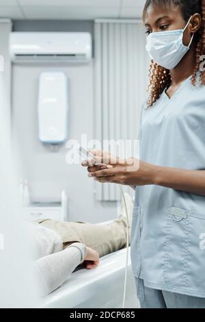 Die Hände der jungen Assistentin in der medizinischen Uniform und Maske Über das Bedienfeld Stockfoto
