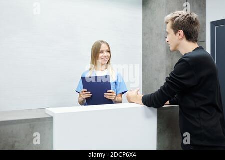 Glückliche junge Assistentin oder Rezeptionistin in blauer Uniform in der Hand Zwischenablage Stockfoto